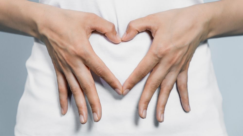 young woman who makes a heart shape by hands on her stomach | Feature | 12 Best Anti-Aging Foods For Gut Health